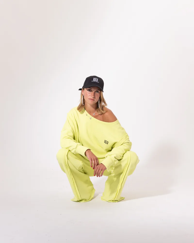 Ensemble jogging vert fluo Licorne Passion en pose accroupie, sweat oversize épaule dénudée